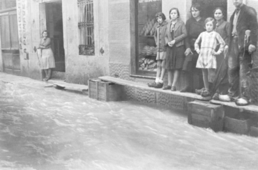 Inundació de Banyoles a causa del desbordament de l'estany. Habitants sobre taulons de fusta davant d'una fleca a un carrer inundat