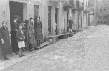Inundació de Banyoles a causa del desbordament de l'estany. Carrer inundat i habitants davant la fleca