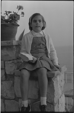 Nena asseguda en un mur davant del mar